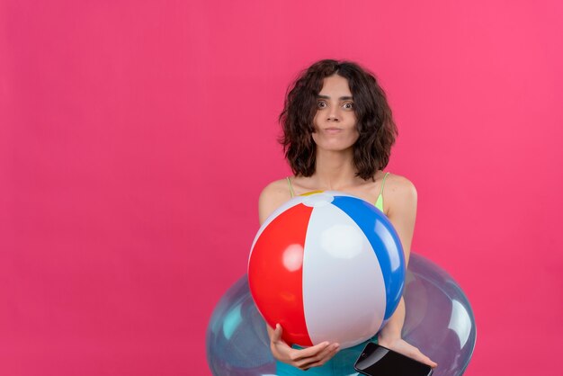 Una giovane donna positiva con i capelli corti in top verde raccolto sorridente e tenendo palla gonfiabile