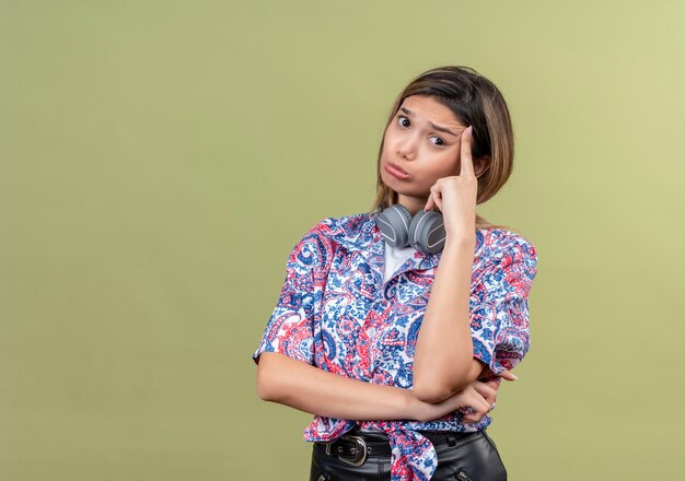 Una giovane donna premurosa che indossa la camicia stampata paisley nel pensiero delle cuffie