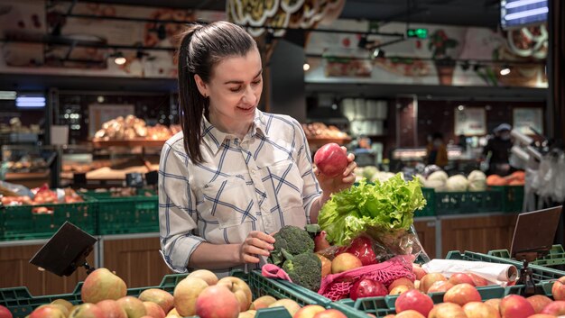 Una giovane donna sceglie frutta e verdura in un supermercato