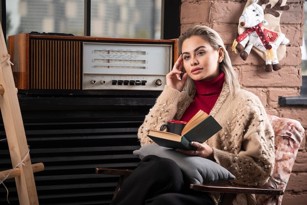 Una giovane donna seduta con un libro e bere caffè