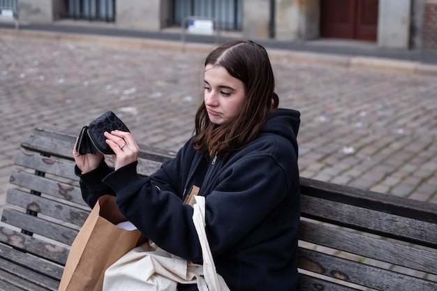 Una giovane donna si siede su una panchina con un concetto di portafoglio vuoto di mancanza di denaro