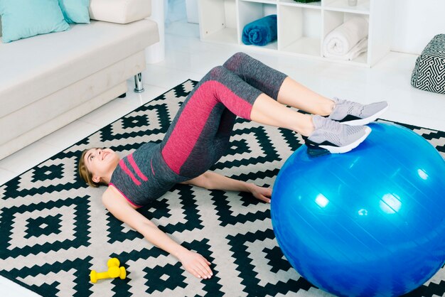 Una giovane donna sorridente attraente che si esercita con la palla di forma fisica su tappeto