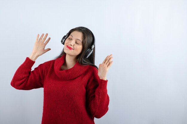 Una giovane donna sorridente con un maglione caldo rosso che ascolta musica in cuffia