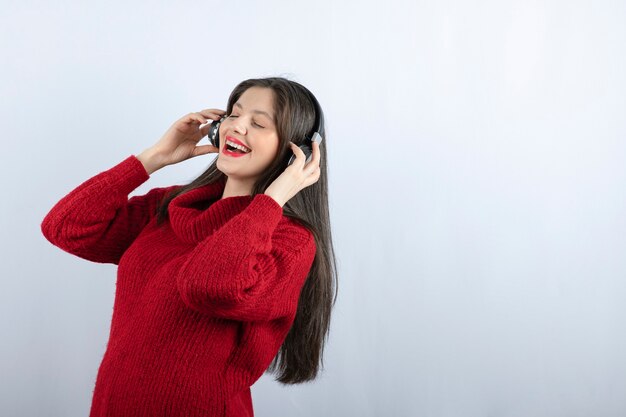 Una giovane donna sorridente con un maglione caldo rosso che ascolta musica in cuffia