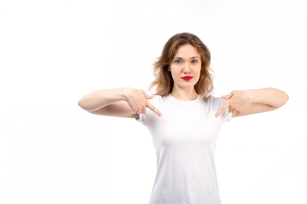 Una giovane donna vista frontale in camicia bianca e jeans moderni neri sottolineando le dita sul bianco