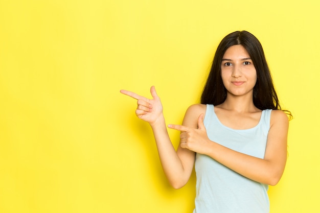 Una giovane donna vista frontale in camicia blu in posa e sottolineando con le dita sullo sfondo giallo ragazza posa modello bellezza giovane