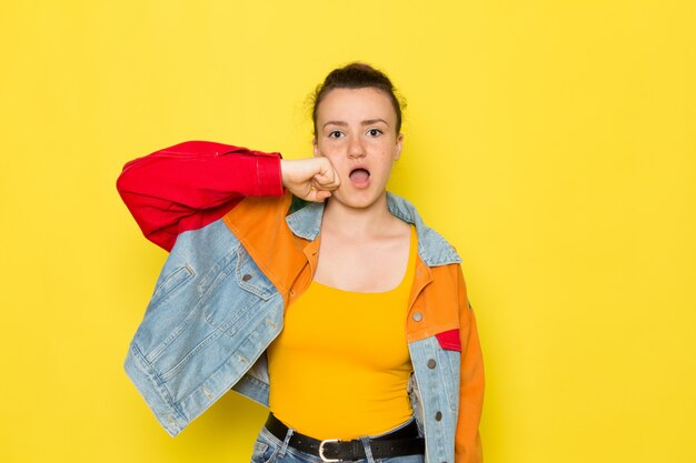 Una giovane donna vista frontale in giacca colorata camicia gialla e blue jeans battendo il viso