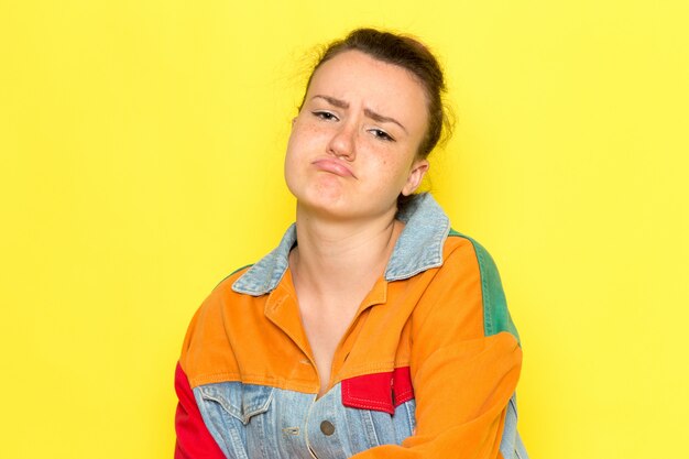 Una giovane donna vista frontale in giacca colorata camicia gialla e blue jeans mostrando con espressione rattristata