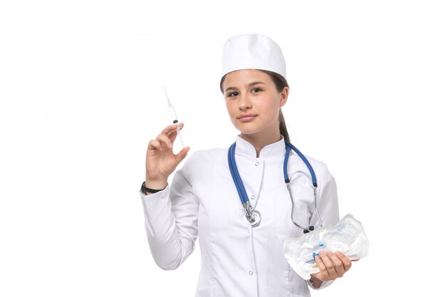 Una giovane dottoressa vista frontale in tuta medica bianca e berretto bianco con iniezione stetoscopio blu