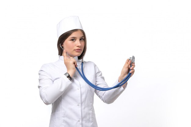 Una giovane dottoressa vista frontale in tuta medica bianca e berretto bianco con stetoscopio blu in posa