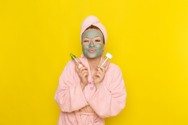 Una giovane e bella donna vista frontale in accappatoio rosa con spray viso azienda maschera