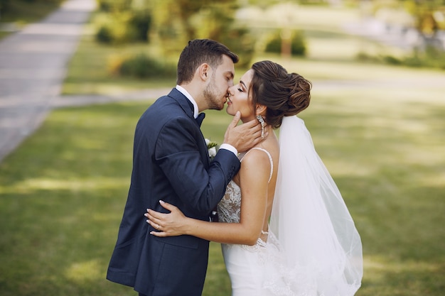 Una giovane e bella sposa e suo marito in piedi in un parco estivo con bouquet