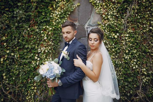 Una giovane e bella sposa e suo marito in piedi in un parco estivo con bouquet