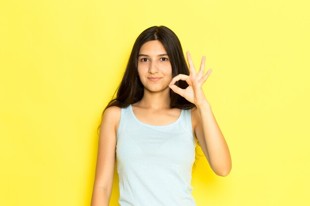 Una giovane femmina di vista frontale in camicia blu che posa sorridendo e mostrando il segno giusto