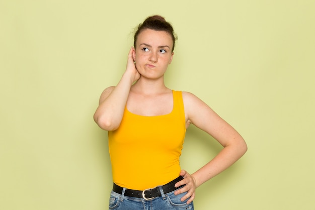 Una giovane femmina di vista frontale in camicia e blue jeans gialle con l'espressione di pensiero