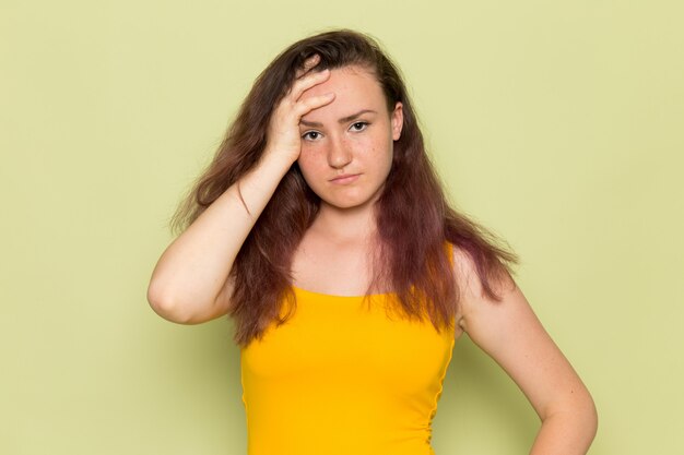 Una giovane femmina di vista frontale in camicia gialla con il mal di testa depresso di emozione della ragazza di espressione