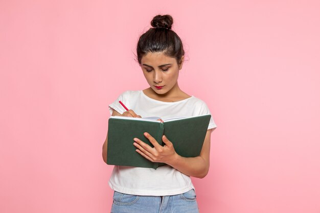 Una giovane femmina di vista frontale in maglietta bianca e blue jeans che annotano le note