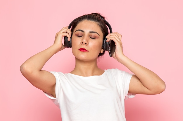 Una giovane femmina di vista frontale in maglietta bianca e blue jeans che ascolta la musica