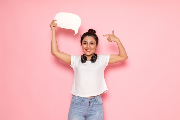 Una giovane femmina di vista frontale in maglietta bianca e blue jeans che tengono segno bianco con il sorriso sul suo fronte