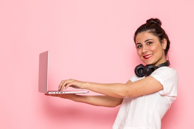 Una giovane femmina di vista frontale in maglietta e blue jeans bianche facendo uso di un computer portatile con il sorriso
