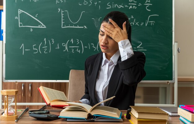 una giovane insegnante scontenta si siede a tavola con materiale scolastico libro di lettura mettendo la mano sulla testa in classe