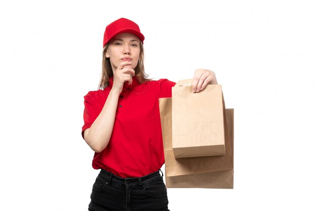 Una giovane lavoratrice femminile del corriere femminile di vista frontale dei pacchetti di consegna della tenuta di servizio di consegna dell'alimento con l'espressione di pensiero su bianco