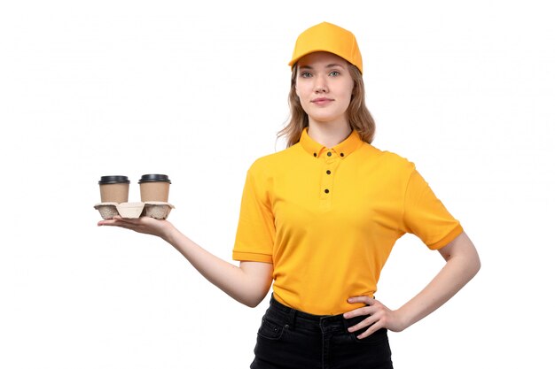 Una giovane lavoratrice femminile del corriere femminile di vista frontale delle tazze di caffè della tenuta di servizio di consegna dell'alimento che sorride sul fondo bianco che consegna l'uniforme di servizio