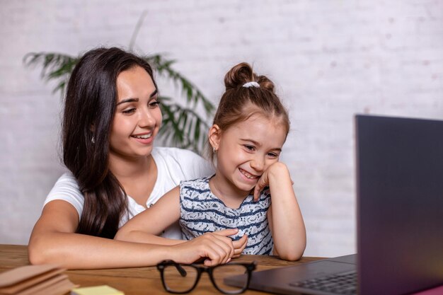 Una giovane madre con la figlia piccola sta acquistando su Internet al personal computer. Concetto di acquisto in linea della famiglia