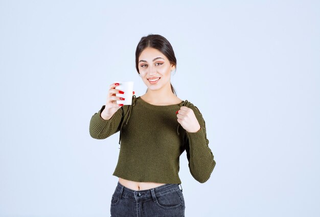 Una giovane modella graziosa che offre un bicchiere di plastica con una bevanda calda.