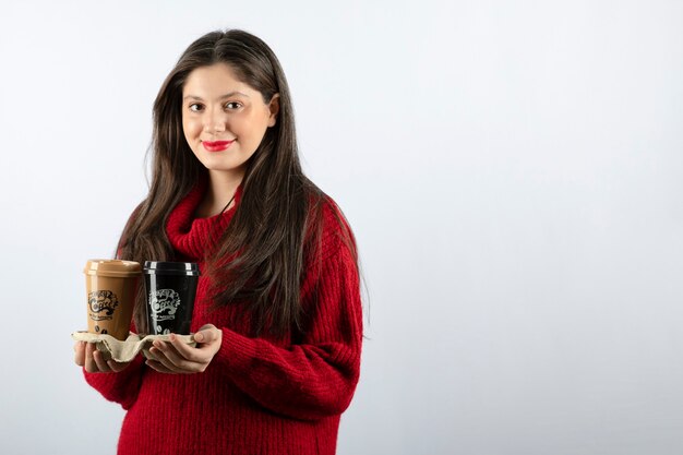 Una giovane modella in maglione rosso con in mano due tazze di caffè
