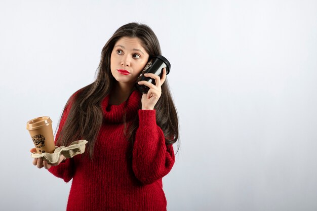 Una giovane modella in maglione rosso con in mano due tazze di caffè