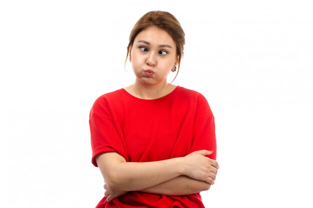 Una giovane ragazza attraente di vista frontale in maglietta rossa che porta i jeans neri che fanno le espressioni divertenti sul bianco
