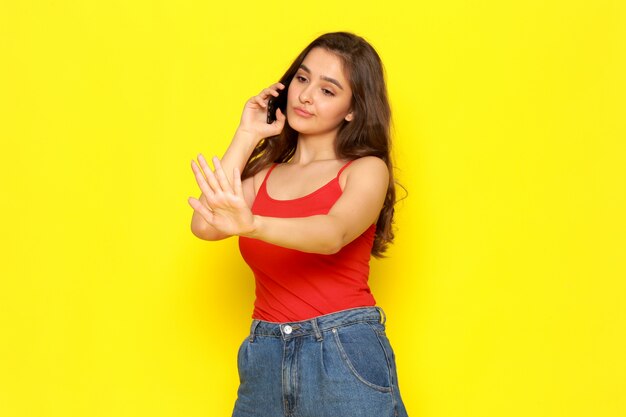 Una giovane ragazza bella vista frontale in camicia rossa e blue jeans, parlando al telefono