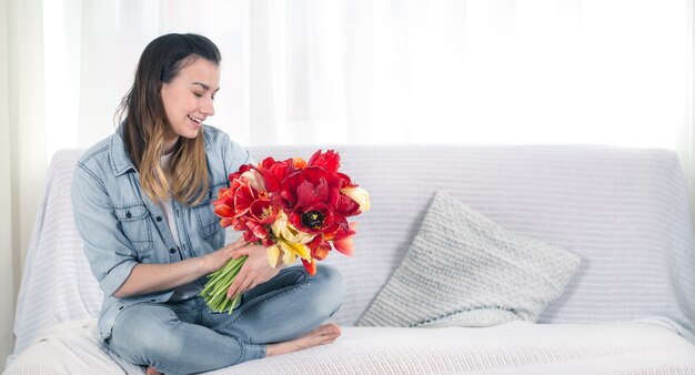 Una giovane ragazza con un grande mazzo di tulipani seduta sul divano del soggiorno.