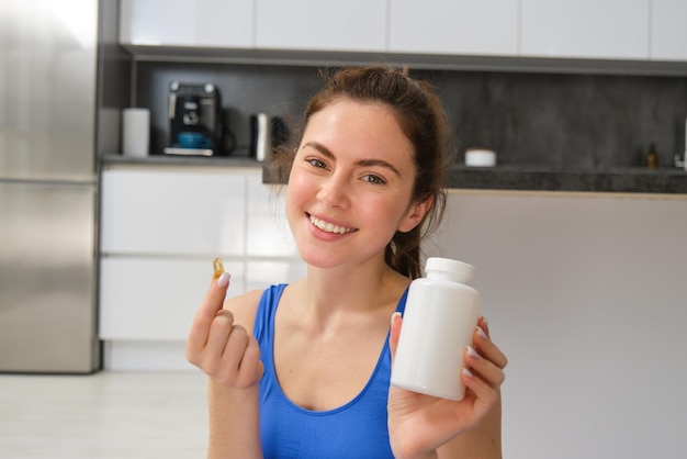 Una giovane ragazza felice e in forma che fa sport a casa mostra integratori alimentari che assumono vitamine per un corpo sano