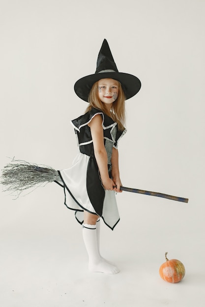 Una giovane ragazza vestita di nero da strega ha in testa un cappello a forma di cono. Ragazza seduta su una scopa e mangia una zucca