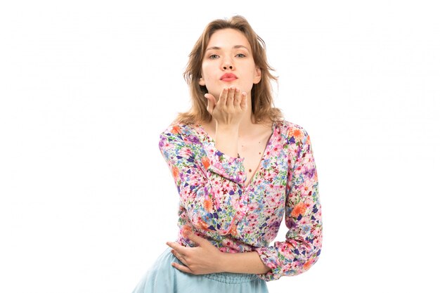 Una giovane signora attraente di vista frontale in camicia colorata fiore progettato e gonna blu in posa inviando baci d'aria sul bianco