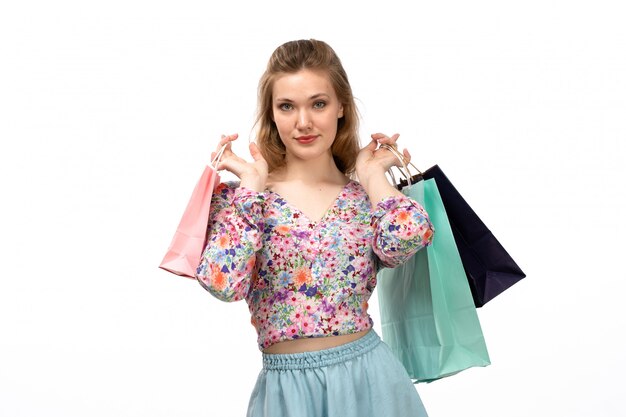 Una giovane signora attraente di vista frontale in camicia variopinta progettata fiore e pacchetti blu che tengono i pacchetti di acquisto sul bianco