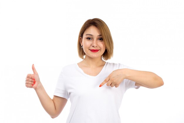 Una giovane signora di vista frontale in camicia bianca che posa mostrando sorridente come il segno sul bianco