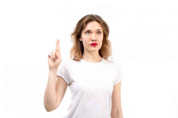 Una giovane signora di vista frontale in camicia bianca e jeans moderni neri che posano pensando sul bianco