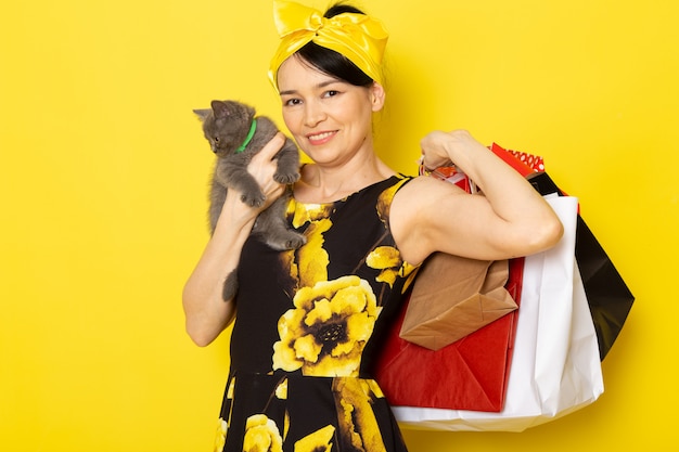 Una giovane signora di vista frontale in fiore giallo-nero ha progettato il vestito con la fasciatura gialla sui pacchetti di acquisto della tenuta della testa e sul gattino sul giallo
