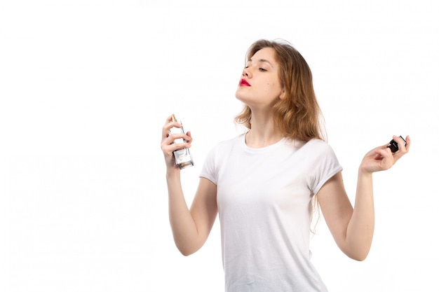 Una giovane signora di vista frontale in maglietta bianca facendo uso del tubo nero del profumo sul bianco