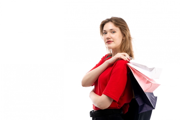 Una giovane studentessa di vista frontale in pacchetti rossi di acquisto della tenuta della borsa nera della camicia rossa sul bianco