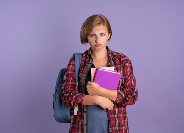 Una giovane studentessa slava scontenta che indossa uno zaino tiene un libro e un taccuino
