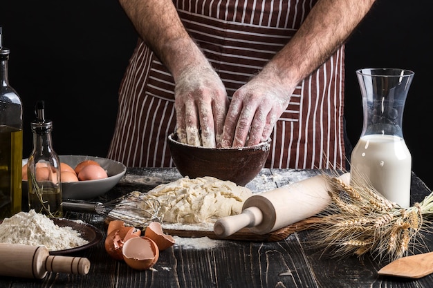 Una manciata di farina con uovo su una cucina rustica. Sullo sfondo delle mani degli uomini, impastare la pasta. Ingredienti per la cottura di prodotti farinacei o impasti pane, muffin, crostate, impasti per pizza. Copia spazio