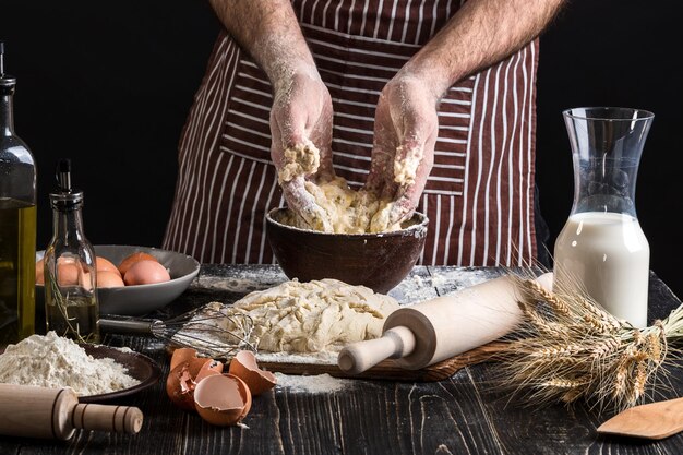 Una manciata di farina con uovo su una cucina rustica. Sullo sfondo delle mani degli uomini, impastare la pasta. Ingredienti per la cottura di prodotti farinacei o impasti pane, muffin, crostate, impasti per pizza. Copia spazio