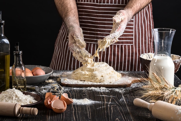 Una manciata di farina con uovo su una cucina rustica. Sullo sfondo delle mani degli uomini, impastare la pasta. Ingredienti per la cottura di prodotti farinacei o impasti pane, muffin, crostate, impasti per pizza. Copia spazio