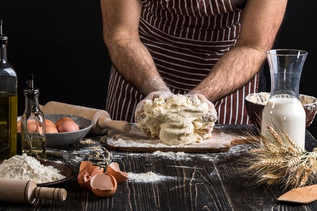 Una manciata di farina con uovo su una cucina rustica. Sullo sfondo delle mani degli uomini, impastare la pasta. Ingredienti per la cottura di prodotti farinacei o impasti pane, muffin, crostate, impasti per pizza. Copia spazio