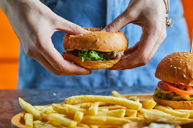 Una mano di donna che tiene cheeseburger con patate fritte, ketchup, maionese