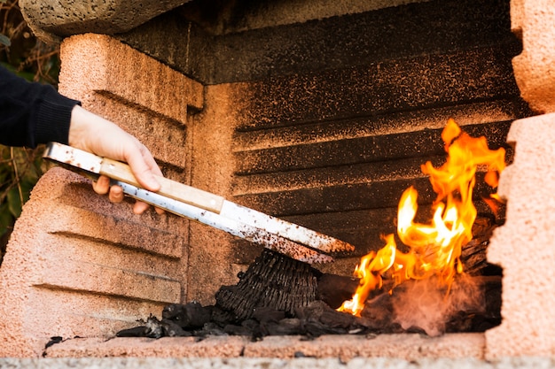 Una mano di persona che brucia carbone con tong in firepit